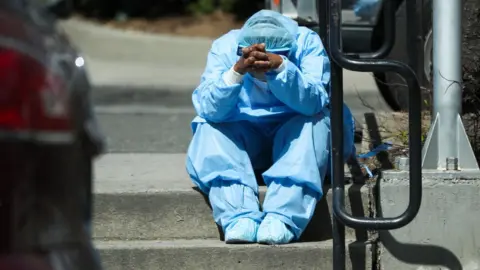 Getty Images A tired healthcare worker is seen by the Brooklyn Hospital Center in New York, United States on April 1, 2020