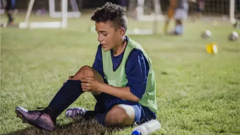 Getty Images A young football player sitting on the ground looking at his leg