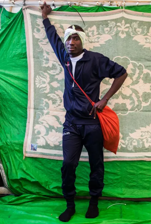 Marcus Drinkwater Amin Dada leans against the background and poses