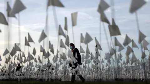 Getty Images A man in a mask walks among flags representing those that died from Covid