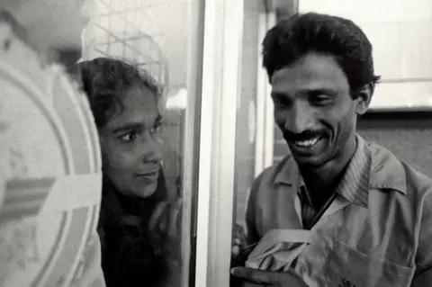 BBC A woman looks at her husband through a window at Dhaka airport