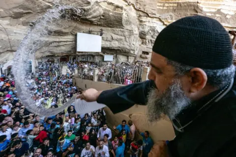 KHALED DESOUKI/AFP Coptic Orthodox priest sprinkles holy water on gathering worshippers.