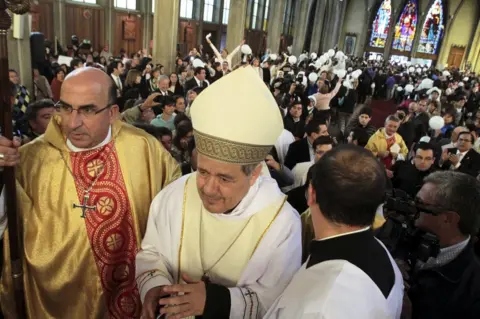 Reuters Bishop Juan Barros (C) attends his first religious service as people protest against him at the Osorno cathedral, south of Santiago, Chile, 21 March 2015