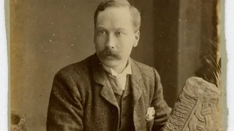 MNH PMC Kermode holding a piece of a Manx stone cross