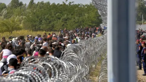 EPA Migrants walk along the border fence between in Horgos, Serbia, 15 September 2015