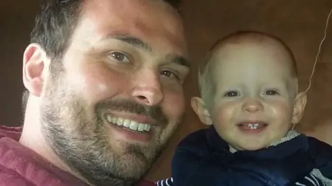 James Cook A picture of a father and baby boy smiling into the camera.