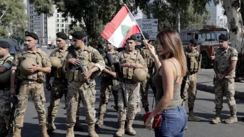 AFP/Getty Images A woman waves a Lebanese flag in front of soldiers in Tripoli, Lebanon. Photo: 22 October 2019