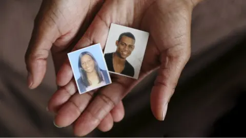 Caritas Magaly Henriquez holds up photos of her two youngest children