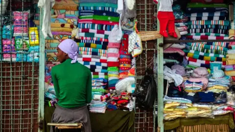 Getty Images A vendor sits at a stall selling cloth towels, hats and other textiles in the Zimbabwean capital Harare on November 16, 2017