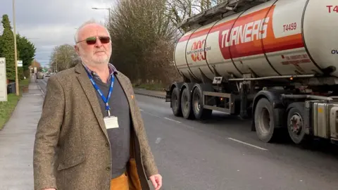 Jill Bennett/BBC Cllr Jim Moriarty standing at side of A10 in West Winch