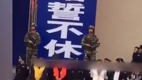 Beijing News Armed police stand behind a group of people waiting to hear criminal sentences