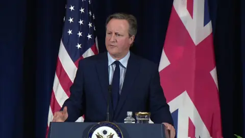 David Cameron speaking at a dais with the US and UK flags behind him