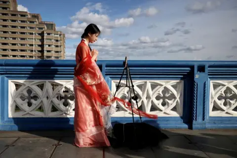 Kevin Coombs / Reuters A Chinese student who calls herself Evie makes a video for her followers on Douyin, Tower Bridge in London