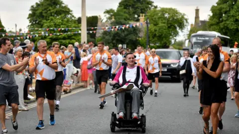 Getty Images Baton bearer Stephen Murray carries the Queen's Baton during the Birmingham 2022 Queen's Baton Relay at a visit to Broadway on July 22, 2022 in Worcestershire