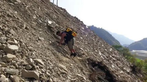 We Care Solar Man climbing rubble in earthquake aftermath with yellow solar suitcase strapped to his back