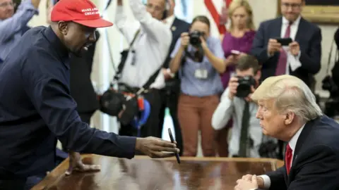 Reuters Rapper Kanye West shows a picture of a plane on a phone to US President Donald Trump during a meeting in the White House Oval Office, 11 October 2018