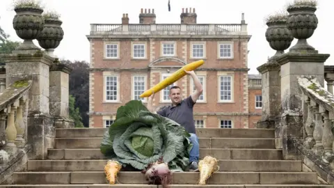 PA Media Paul Proud with with his winning giant cabbage, parsnip, carrot, beetroot