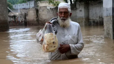 Getty Images A man wades through a flooded area in Peshawar, Khyber Pakhtunkhwa, Pakistan on August 27, 2022