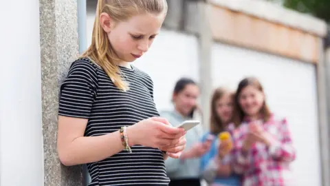 Getty Images Teenage girl holding a phone being bullied