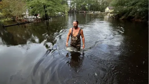 Getty Images Man wades through thigh-high floodwater in neighbourhood