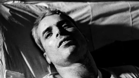 Getty Images This file picture taken in 1967 shows US Navy Airforce Major John McCain lying on a bed in a Hanoi hospital as he was being given medical care for his injuries.