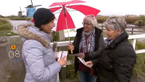 NOS Jeugdjournaal Kinderdijk inhabitant hands cards to tourists, Netherlands