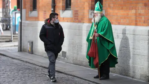 Niall Carson A man dressed as St Patrick watching a man with a mask walk by in Temple Bar, Dublin