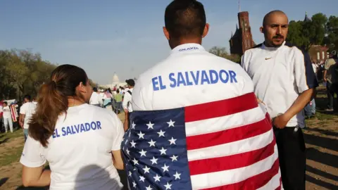 Getty Images A protester wearing T-shirt that reads El Salvador and with a US flag draped over his shoulders during an immigration rally on the National Mall 10 April 2006 in Washington