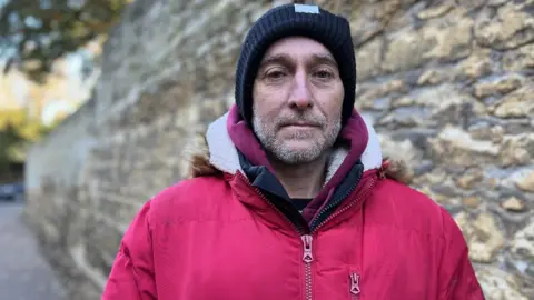 Emma Baugh/BBC Head and shoulders of man with wall behind