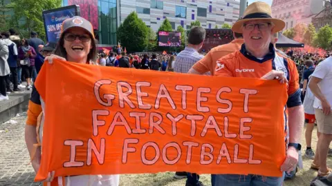 Alex Pope/BBC Joanne Stuckey and Tim Hayden holding up a "Greatest Fairy-tale In Football sign"