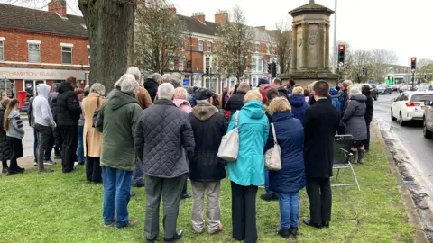 Martin Heath/BBC Crown of people gathered around a stone monument at a busy road junction