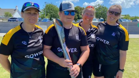 woman holding queen's baton with team mates