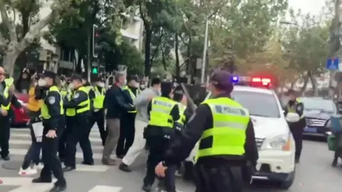 BBC Police officers wearing fluorescent jackets confront protesters next to a vehicle in Shanghai