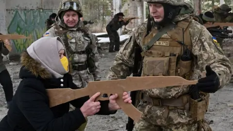 SERGEI SUPINSKY A woman holds a cardboard replica of a Kalashnikov rifle in a military drill outside Kyiv on 19 February 2022