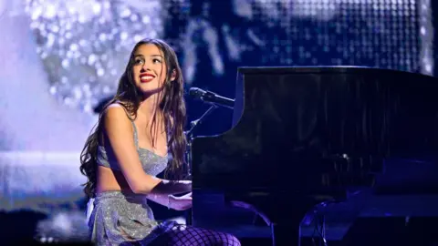 Getty Images Rodrigo smiles at the crowd as she plays piano on stage