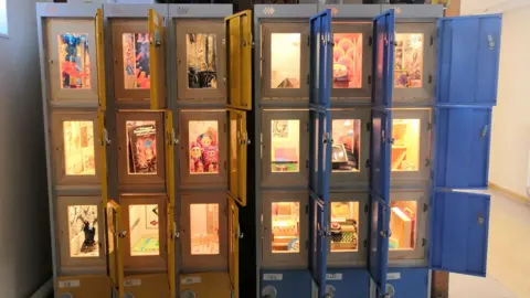 The lockers at The Rumble Museum displaying a variety of toys such as Russian nesting dolls, a typing machine and a Monopoly set.