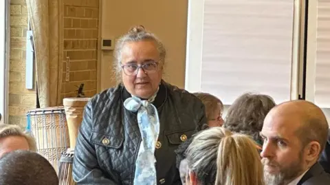 Cad Taylor/BBC Gulshan Kayembe overlooks a table of people a community networking event.