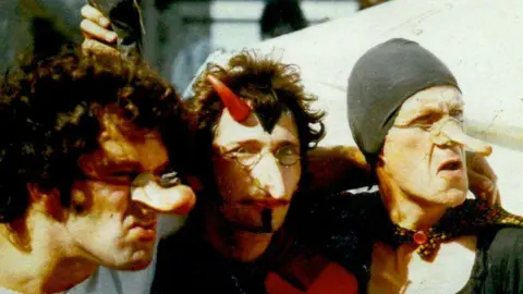 Miracle Theatre An old photo of three people with long nose props.