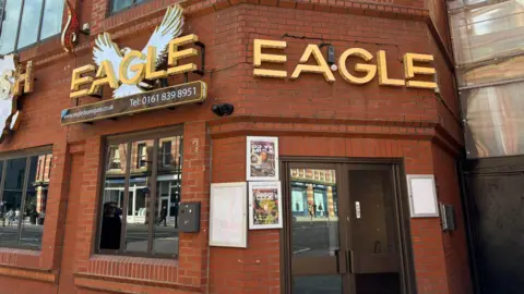 A red brick building with brown framed windows and door. Eagle is written on the front in gold letters 