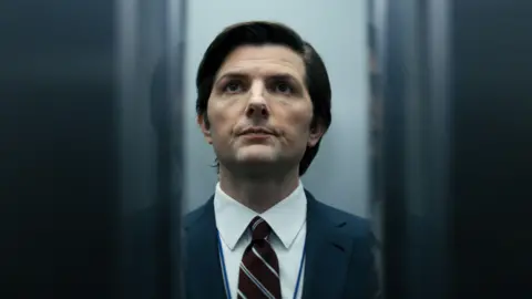 Getty Images El actor Adam Scott sostuvo en un ascensor cuando las puertas se cierran. Entre las puertas de la cerca, podemos ver que lleva un disfraz y corbata agudos. Está afeitado y tiene el cabello negro bien mantenido.