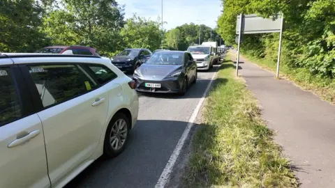 Two lanes of traffic are queued back up a hill with some drivers reporting delays of up to two hours.