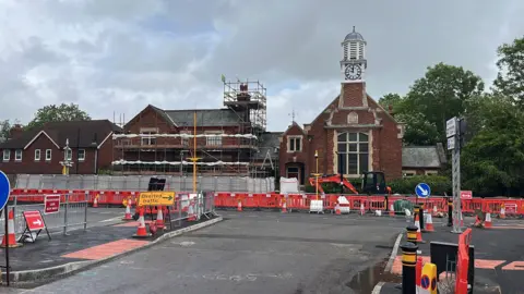 George Carden/BBC Plastic fencing and cones set up with fencing and an excavator in front of the old court house which has a large front window and clock tower