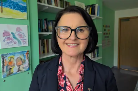 Amanda Pithouse, a woman with a dark bob, wearing glasses, smiling at the camera
