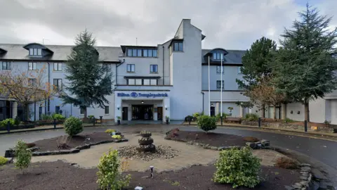 Google The front of the Hilton Hotel in Templepatrick, with a fountain in the foregound and a small roundabout. The hotel's entrance can be seen under a sign of the hotels name written in blue lettering.