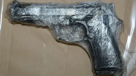 PSNI A black handgun wrapped in plastic is set on top of brown paper.