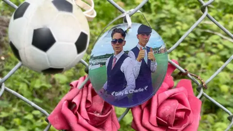 BBC A football, roses and a photo of the two boys who died, at the scene of the crash