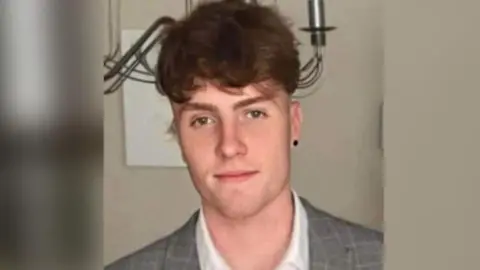 Tom Linton in a white shirt and grey suit jacket. He has brown hair and brown eyes.