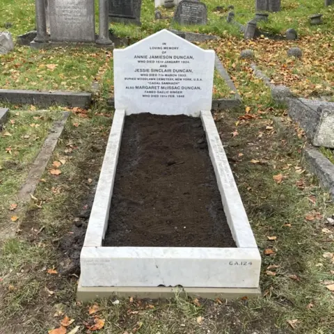 Còisir Lunnainn The gravestone is a pristine white with clearly defined black lettering. Slabs of stone have also been placed around the grave.