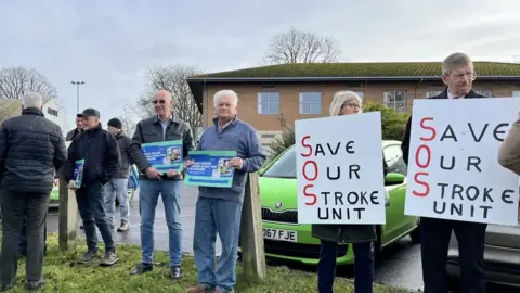 Protestors holding placards saying "save our stroke unit"