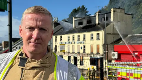 A member of the Northern Ireland Fire and Rescue Service stood in front of a burnt building